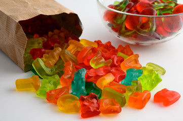 Glass bowls and paper bag of colorful gummy candies on white backgroundGlass bowls and paper bag of colorful gummy candies on white background