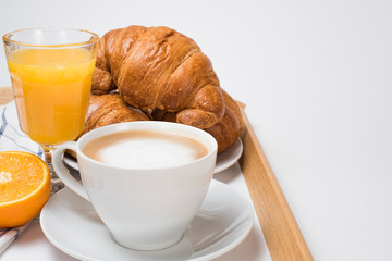 Breakfast coffee with croissants and orange juice on a white background. Latte on a saucer and cellular cotton towel on a wooden tray