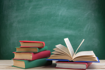 Education and reading concept - group of colorful books on the wooden table in the classroom, blackboard background