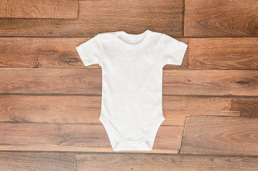 Top view white baby bodysuit on wooden background. Copy space for text lettering