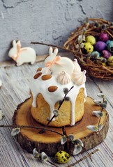 Easter cake in the form of a rabbit on a tree cut, table decorated with rabbits, against the background of a basket with multi-colored quail eggs