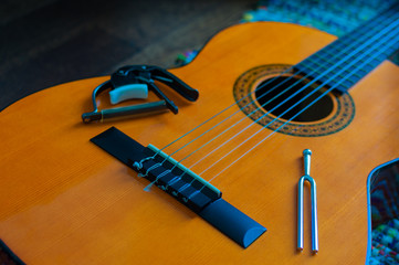 Closeup of spanish wooden guitar of orange and brown tones, with nylon strings, guitar nut and tuning fork