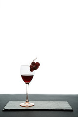 Glass of red wine garnished with grape on white background