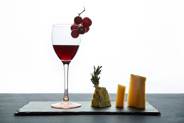 Glass of red wine garnished with grape and pieces of savory cheese