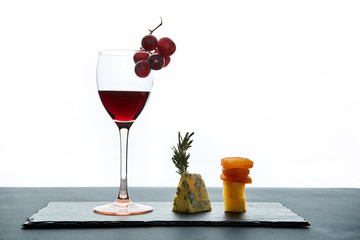 Composition of traditional aromatic cheese and dried apricots with glass of red wine on white background