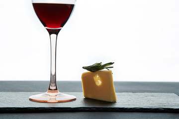 Glass of red wine garnished with grape and piece of savory hard cheese on slate dish