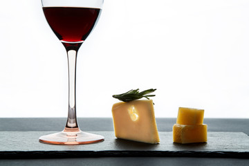 Glass of red wine garnished with grape and pieces of savory hard cheese