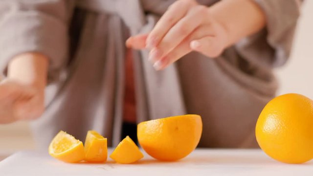 Woman in bathrobe cutting orange. Taking slice going away. Healthy nutrition eating weight loss habit breakfast lifestyle.
