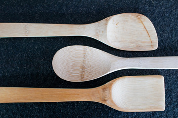 Three wooden kitchen spoons on a black marble table. Useful utensils for cooking, cooking equipment...