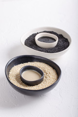 Black tahini and white tahini sauce in bowls on white background. Natural paste made from sesame seeds. Copy space.