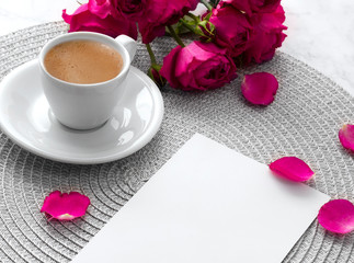 Pink roses with blank greeting card and coffee cup over pink marble background. 