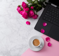 Feminine workspace with laptop computer, bouquet of roses and coffee on a marble table. 