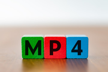 Three colorful wooden cubes with the lettering MP4 as a symbol for video files on a wooden table 