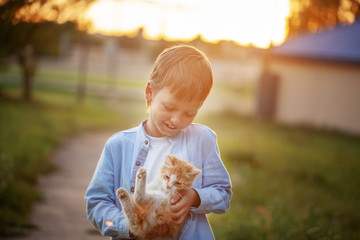 Happy kid with a kitten in his hands in nature on summer.