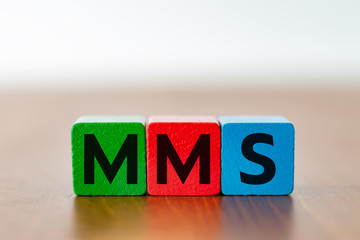 Three colorfull wooden cubes with the lettering MMS on a wooden table 