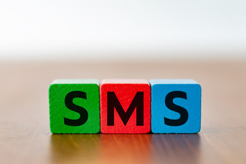 Three colorful wooden cubes with the lettering SMS on a wooden table 