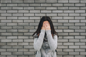 Beautiful woman on the gray background with sad expression covering her face with hands while crying. Depression concept.