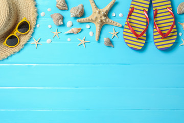 Straw hat, sunglasses, flip flops and many starfishes on color wooden background, space for text...