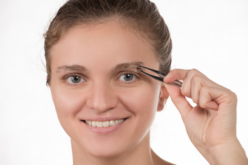 Young girl pulls out her eyebrows with tweezers metal on a white background