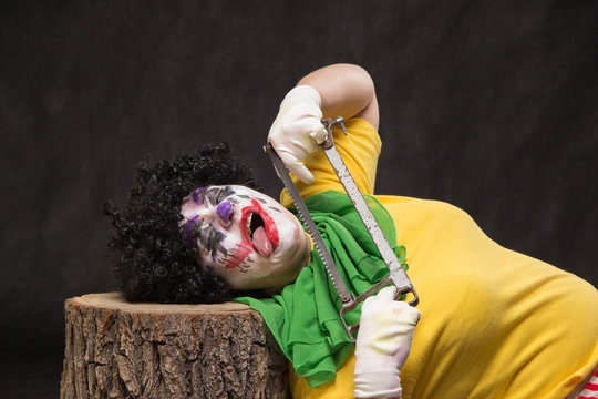 Scary clown with an ugly smile and saw on a black backgroun