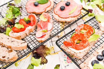 Different sandwiches for breakfast on a white wooden background. Crackers with prawns, vegetables, cheese and ham.