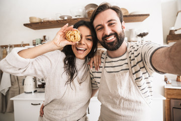 Portrait of joyful couple taking selfie photo while cooking in kitchen at home