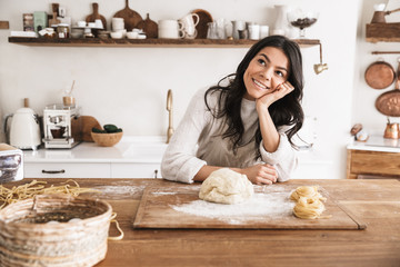 Portrait of smiling european woman making homemade pasta of dough in kitchen at home