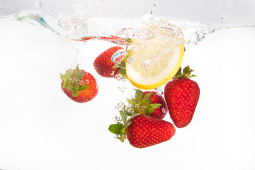Strawberries and lemon slice splashing in to water on the white