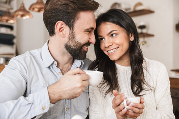 Portrait of loving european couple drinking coffee while having breakfast in kitchen at home
