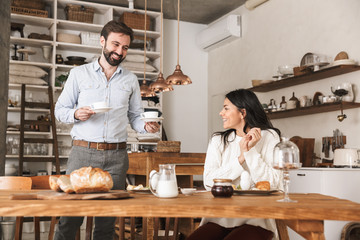 Portrait of beautiful young couple drinking coffee while having breakfast in kitchen at home