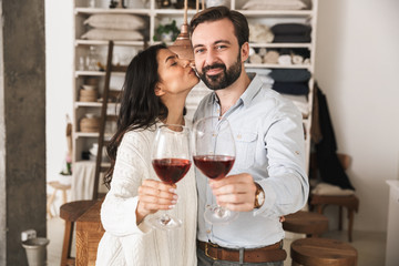 Portrait of joyous european couple drinking wine from glasses while having romantic dinner at home