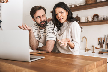 Portrait of pretty couple looking at laptop while cooking pastry in kitchen at home