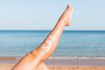 Raised up female leg with spf word made of sun cream at the beach. Sun protection factor concept