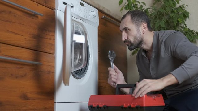 The breakdown of the washing machine. A man with an adjustable wrench looks into a broken washing machine.
