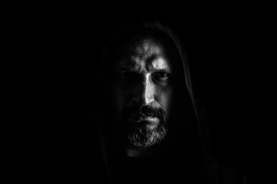 Brutal man with a gray beard in the hood with sharp shadows on a black background. Copy space.