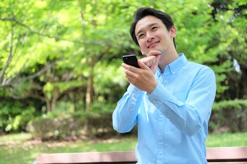 公園でスマホ　携帯を操作する三十代男性