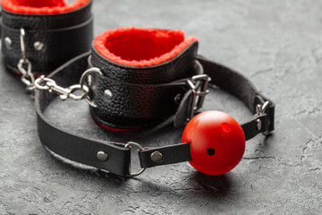 BDSM sex toys for adults. Gag with red ball and handcuffs on black background.