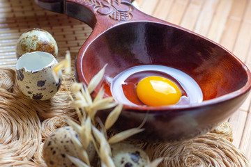 Fresh raw quail eggs in wooden spoon on rustic straw and wooden vintage background.