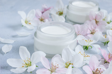 Fototapeta na wymiar Beauty pastel concept skin face care. Composition of a jar of cream and bloomed spring flowers.