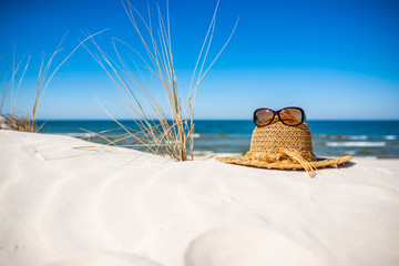 Sunny holiday beach, summer vacation concept - sun hat and sunglasses on white sand, Baltic Sea, Poland - obrazy, fototapety, plakaty