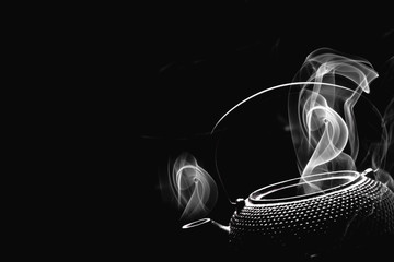Teapot with boiling water. Steaming tea kettle on black background. Cooking concept.
