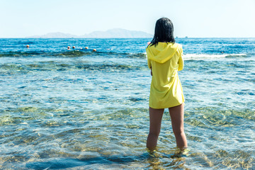 Travel and leisure, a girl with black hair in a yellow jacket stands against the blue sea