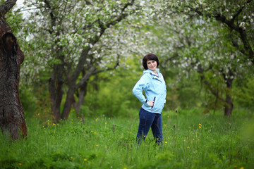 Beautiful mature woman posing for the camera in the spring garden. The girl enjoys the flowering of apple trees.