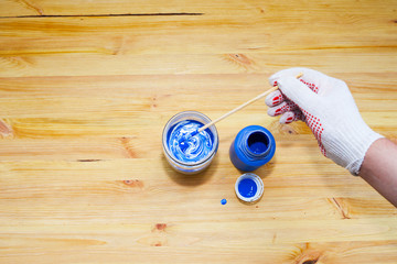 Adding blue dye to a jar of white paint. Men's gloved hand, wooden background. Painter