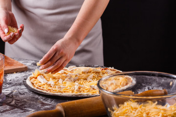 young woman in a gray aprons prepares a Hawaiian pizza