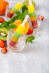 Striped popsicle with different flavors, mango, orange, kiwi and strawberry in glass cups. Summer food concept with copy space.