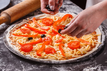 young woman in a gray aprong prepares a vegetarian pizza