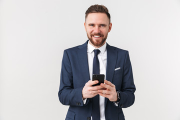Happy young handsome businessman posing isolated over white wall background using mobile phone.