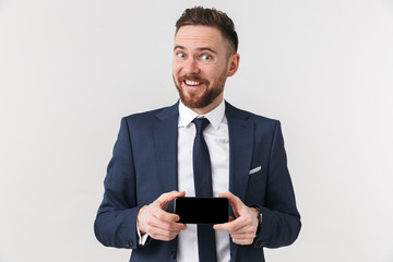 Happy young handsome businessman posing isolated over white wall background showing display of mobile phone.