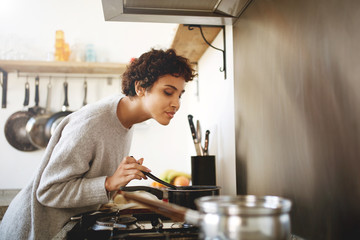 young woman cooking and smelling food from pot